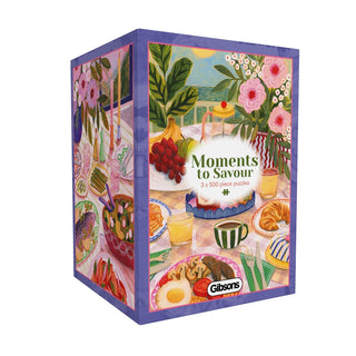 The “Moments To Savour | 3 x 500 Piece Jigsaw Puzzle” set from Gibsons Games includes three beautifully illustrated puzzles, each with 500 pieces and showcasing charming scenes of food, flowers, and table settings by a talented UK artist. Crafted from recycled cardboard for an eco-friendly experience, the Gibsons Games brand is featured on the box.