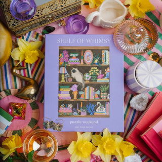 Puzzle Weekend’s Shelf of Whimsy | 1,000 Piece Jigsaw Puzzle features a delightful Danish pastel scene with a bookshelf on a table surrounded by vibrant flowers, glassware, books, and charming decor.