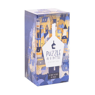 A box set labeled Puzzle in A Bottle by Trevell contains 12 mini jigsaw puzzles, each with 99 pieces. The packaging features illustrated cityscapes in blue and yellow tones, making these charming mini puzzles a perfect gift or collectible.
