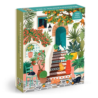 Galison’s Mediterranean Cats 1,000 Piece Jigsaw Puzzle features a charming courtyard scene with a cat, potted plants, stairs, and colorful outdoor furniture.