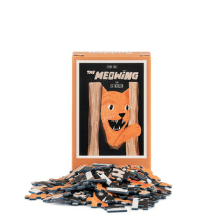 A box labeled The Meowing | 99 Piece Mini Jigsaw Puzzle by Happily Jigsaw Puzzles, inspired by Nia Gould’s charming style, features artwork reminiscent of The Meowing movie poster: an orange cat peeking out from behind wooden planks, set just beyond a pile of loose mini jigsaw puzzle pieces.