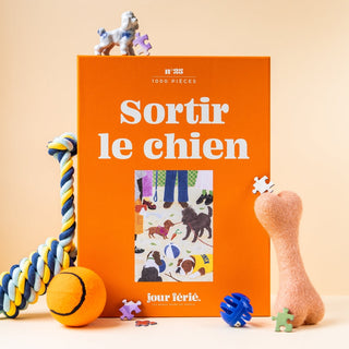Jour Férié Sortir le chien 1,000 piece jigsaw puzzle, made in France, features an orange box and is pictured with dog toys like a rope, ball, plush bone, and small dog figurines.