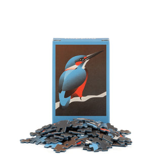 A box displaying an illustrated kingfisher stands behind a scatter of mini jigsaw pieces on a white background—Happily Jigsaw Puzzles’ King Fisher | 99 Piece Mini Jigsaw Puzzle makes a charming gift for bird lovers.