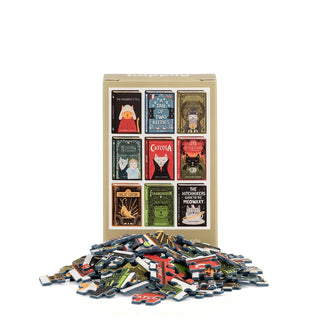A box of the “Book Cats | 99 Piece Mini Jigsaw Puzzle” by Happily Jigsaw Puzzles, adorned with illustrated cat-themed book covers, stands behind a pile of loose jigsaw puzzle pieces on a white background.