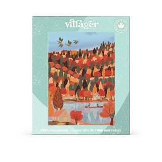 A Villager Puzzles “Changing Seasons” 1,000-piece jigsaw puzzle box featuring artwork by Marie-Laure Plano, depicting autumn trees, charming houses, a lake with two people canoeing, and birds in flight.