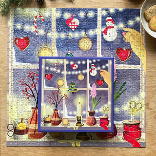 The ViSSEVASSE "Christmas Window" 500 Piece Jigsaw Puzzle depicts a joyful holiday window scene, with its square box—featuring coordinating artwork—placed in the center and partially covering the completed puzzle. Made from FSC-certified materials, this delightful puzzle is sure to bring festive cheer to any holiday gathering.