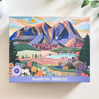 The Mountains & Valleys | 1,000 Piece Jigsaw Puzzle by Spaghetti Tree features a colorful illustrated mountain landscape inspired by Utah, with flowers in the foreground.