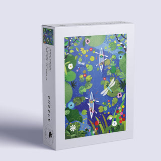 The Das Puzzle Kollektiv Canopy Canoeing 1,000 Piece Jigsaw Puzzle comes in a plastic-free rectangular box featuring vibrant art of two kayaks on a blue river, surrounded by greenery, flowers, and a dragonfly.
