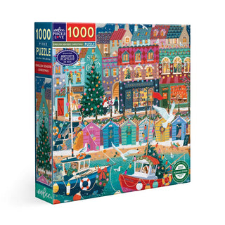 The eeBoo English Seaside Christmas 1,000 Piece Jigsaw Puzzle features a vibrant holiday scene with boats, decorated homes, Christmas trees, lights, and ornaments by the sea.