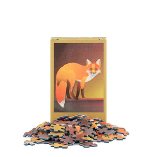 Behind scattered Fox Puzzle pieces on a white background, a box from Happily Jigsaw Puzzles featuring an illustrated fox invites you to assemble the delightful Fox | 99 Piece Mini Jigsaw Puzzle.