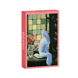 The Rêveur Bleu 99 piece jigsaw puzzle by Olleo Puzzles features a white cat on a windowsill with flowers and an open book, set against stunning stained glass windows.