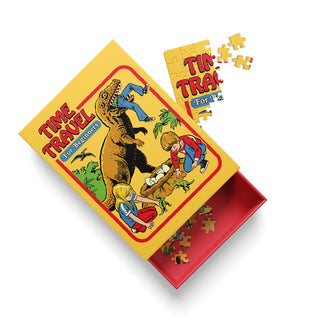 Ohh Deer’s Time Travel | 99 Piece Jigsaw Puzzle comes in a yellow box labeled “Time Travel for Beginners,” featuring an illustration of children and a dinosaur. The nostalgic design showcases classic retro jigsaw styling reminiscent of Steven Rhodes puzzles, with some puzzle pieces and the lid visible.