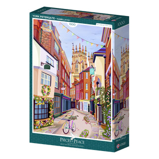 The York Petergate | 1,000 Piece Jigsaw Puzzle by Pieces & Peace features an illustrated York street scene with colorful buildings, a church tower, bunting, and a bicycle. Made in France.
