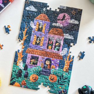 The Spaghetti Tree "Spooky Manor" is a 150-piece Halloween jigsaw puzzle with a haunted house, ghosts, skeletons, pumpkins, and a purple moon. Some pieces are missing and others are scattered around this portable puzzle.