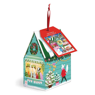 Presented by Galison, the Holiday Market | 130 Piece Jigsaw Puzzle Ornament comes in a house-shaped box adorned with festive holiday illustrations, cheerful animal characters, and a red ribbon handle. The attached tag displays the finished puzzle image, making this charmingly decorated box both an ideal holiday gift and a delightful ornament for the season.