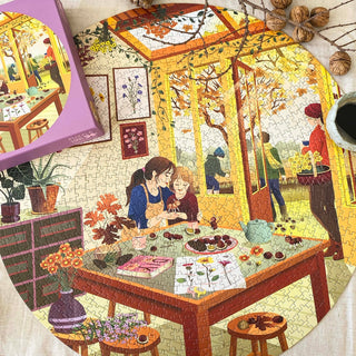 A finished Chestnut Season | 1,000 Piece Jigsaw Puzzle by ViSSEVASSE displays people savoring tea and pastries inside, with colorful autumn foliage visible through expansive windows; the FSC-certified puzzle box and a coffee cup are placed nearby.
