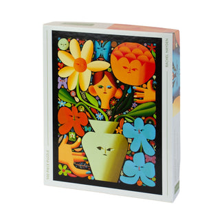 The Kinstler Puzzles "Self Portrait As A Florist" 500 piece jigsaw puzzle showcases Rachel Hayden's vibrant, symmetrical flowers and faces in a vase on a black background. Her name is printed on the box edge.
