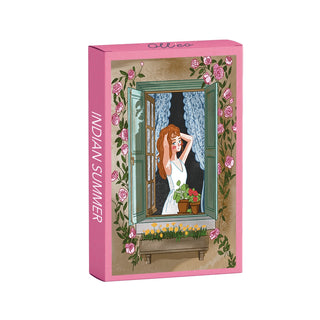 A pink box labeled “Indian Summer | 99 Piece Jigsaw Puzzle” by Olleo Puzzles features an illustration of a woman at an open window surrounded by pink roses and potted flowers. This charming puzzle is perfect for cozy autumn afternoons.