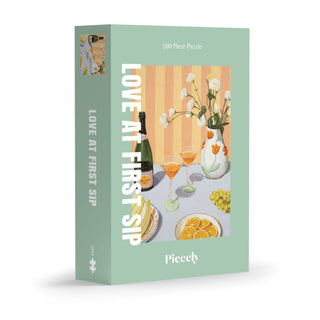 Love At First Sip | 500 Piece Jigsaw Puzzle by Piecely features textured paintings of drinks, flowers, oranges, and grapes on a pastel green backdrop—all in plastic-free packaging.