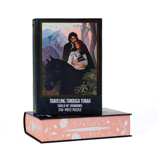 A Traveling Through Turah | 250 Piece Jigsaw Puzzle box stands atop a matching keepsake book box, both decorated with a pink floral and sword design featuring a couple riding a black horse.