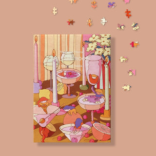 The Puzzle Theory's Mellow Room is a 500-piece jigsaw puzzle designed by Asami Watanabe, featuring a vivid table scene with glassware, candles, flowers, and fruit on a pink background with scattered pieces.