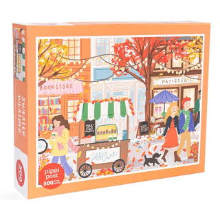 Enjoy the charming "Sweater Weather Cozy Fall Town" 500-piece jigsaw puzzle by Pippi Post, featuring an illustrated box with a vibrant autumn street scene—complete with people, a coffee cart, bookstore, patisserie, swirling fall leaves, and a black cat—for the perfect cozy fall vibes.