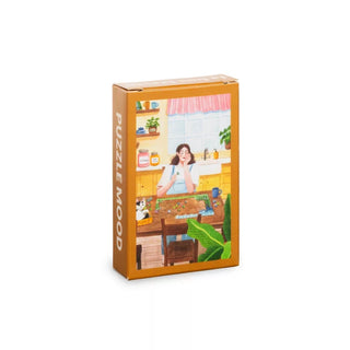 The Trevell Puzzle Mood | 99 Piece Jigsaw Puzzle comes in a rectangular box with an illustration of a woman and her cat assembling a puzzle at the kitchen table.