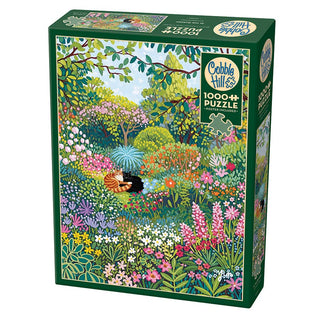 Cobble Hill's "In the Garden" 1,000-piece jigsaw puzzle features a colorful garden scene with flowers, greenery, and a black cat lying in the grass.