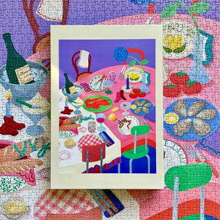 A finished The Evening | 1,000 Piece Jigsaw Puzzle by Das Puzzle Kollektiv, showing a vibrant table with food and drinks; its matching plastic-free box rests atop the completed puzzle.