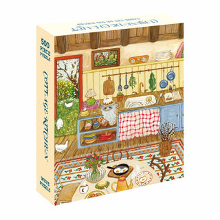 The WEVE Cottage Kitchen | 500 Piece Jigsaw Puzzle features Asia Spettel’s cozy cottage kitchen illustration with a table, sink, shelves, hanging utensils, and assorted kitchen items on a velvet touch puzzle box.