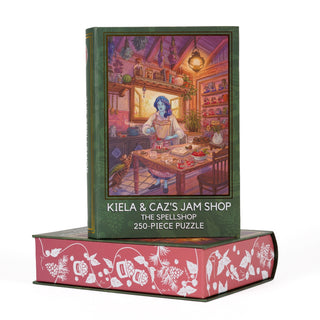 The Kingdom of Threads "Kiela & Caz’s Jam Shop | 250 Piece Jigsaw Puzzle" showcases vibrant artwork of a blue-haired character in a cozy, magical kitchen, all delightfully packaged in a charming book-shaped keepsake box. This inviting fantasy puzzle draws you into a whimsical world where each piece completes an enchanting scene.