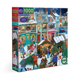 The eeBoo “Holiday Market By the Sea” 1,000-piece puzzle features a festive illustrated holiday market with people, decorated shops, and snowmen in a snowy village scene.