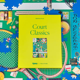 A yellow Court Classics | 1,000 Piece Jigsaw Puzzle box by Piecework Puzzles rests on a half-finished puzzle, displaying vintage tennis equipment and unique sports memorabilia.