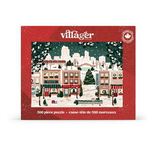 The Small Town Holiday 500 Piece Jigsaw Puzzle by Villager Puzzles features an illustrated snowy town scene on its box, complete with charming shops, a park, and city buildings in the background.