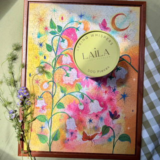 Completed the Laila Luxury Puzzles Spring Whispers 500 Piece Jigsaw Puzzle, featuring vibrant colors and a beautiful floral design, displayed with flowers and the box lid on top.