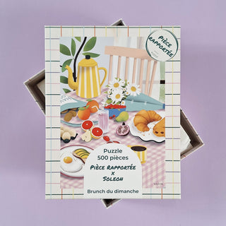 The Brunch Du Dimanche 500-piece jigsaw puzzle by Pièce Rapportée, made in France, features an illustrated brunch scene with foods, flowers, and a yellow teapot on a checkered tablecloth.