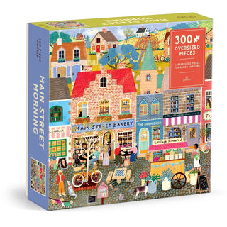 The Galison Main Street Morning 300 Piece Jigsaw Puzzle features a cozy and charming illustration of bustling shops, friendly people, and playful animals along a lively town street. The puzzle includes 300 oversized pieces for easy handling.