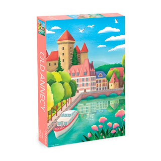 The Olleo Puzzles Old Annecy 1,000 piece jigsaw puzzle features a vibrant scene of the Venice of the Alps, with a castle, riverside buildings, a boat on the water, and pink flowers in the foreground.