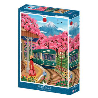 Pieces & Peace's "Fuji Blossoms" is a 500-piece jigsaw puzzle depicting a green train passing cherry blossom trees by Mount Fuji, with a woman in red waiting on the platform. Made in France.