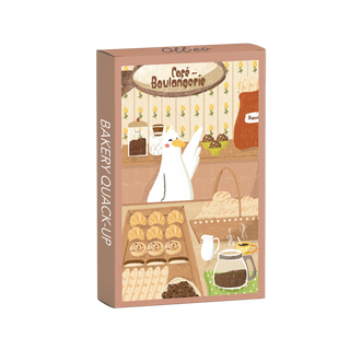Bakery Quack-Up | 99 Piece Jigsaw Puzzle by Olleo Puzzles features Prescilia Swan the duck behind a bakery counter with pastries, bread, coffee, and a Café - Boulangerie sign. Box includes a side label with the puzzle's name and the illustrated scene.