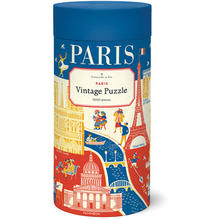 Cavallini & Co. Paris | 1,000 Piece Jigsaw Puzzle comes in a cylindrical tube and features vintage-style illustrations of Paris landmarks like the Eiffel Tower and Notre-Dame in vibrant red, blue, and yellow tones.