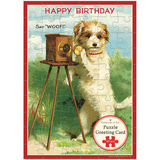 The Cavallini & Co. Happy Birthday Dog 60 Piece Greeting Card Jigsaw Puzzle features a dog on hind legs by a vintage camera, with "HAPPY BIRTHDAY" and "Say WOOF!" above.