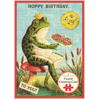 Delightful birthday card: "Happy Birthday Frog" by Cavallini & Co.—a 60 piece jigsaw puzzle featuring a crowned frog on a mushroom, holding flowers beneath a smiling moon.